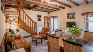 A spacious living room with a wooden staircase, leather sofas, wicker chairs, and a television.
