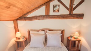 A bedroom with a wooden ceiling, a bed with white linens, two bedside tables with lamps, and a framed picture on the wall.