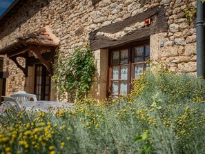 A stone building with a window and a door, surrounded by yellow flowers and greenery. - Child-friendly house with large garden (Prats du Perigord)