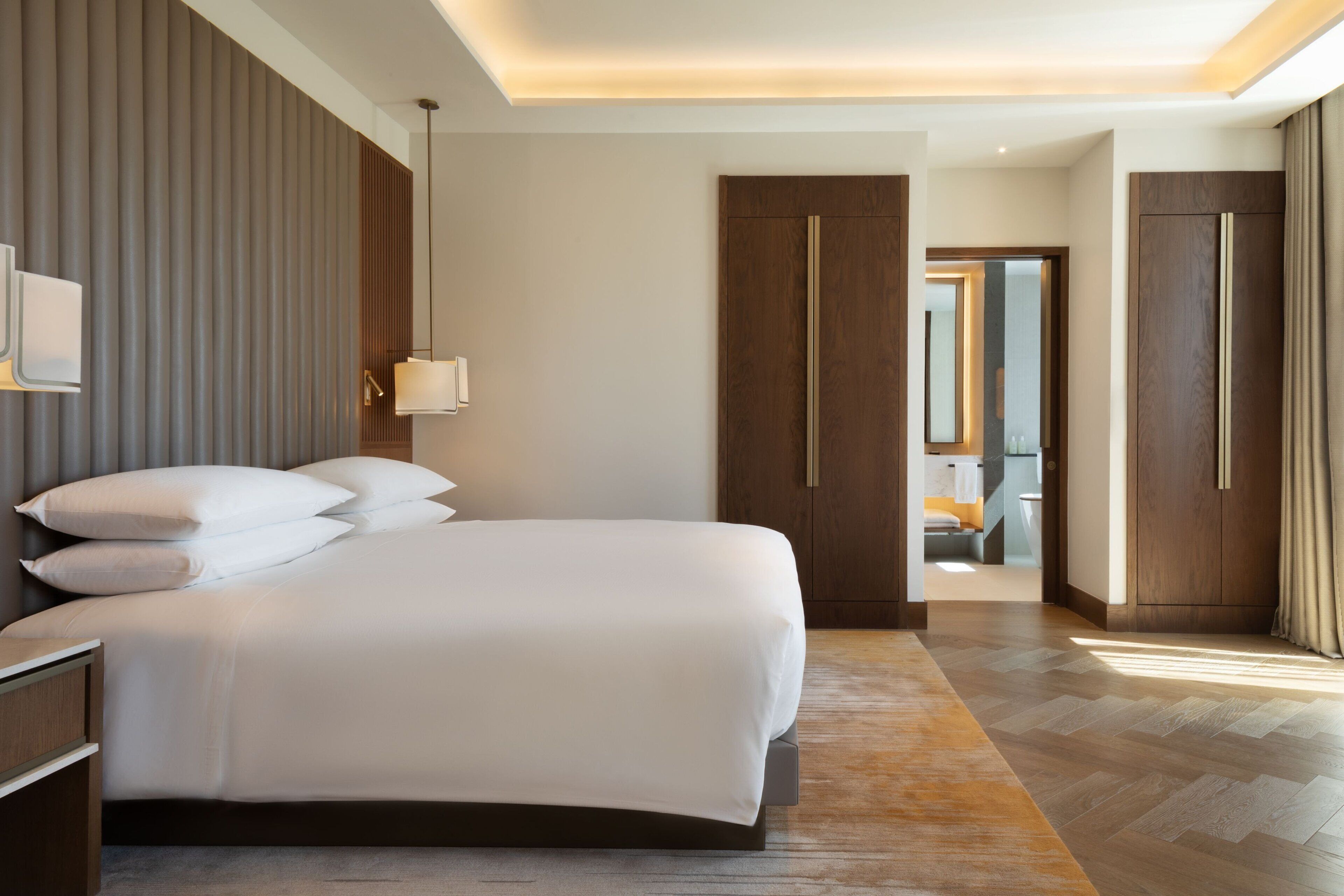 A modern hotel room with a large bed, a bedside table, a wardrobe, and a mirror.
