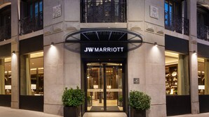 The JW Marriott hotel entrance with a glass facade, illuminated signage, and two potted plants at the entrance. - JW Marriott Hotel Madrid (Madrid)
