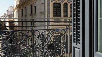 Un balcón con barandillas de hierro forjado ornamentadas y vistas a un edificio clásico con detalles decorativos y fachada azul y dorada.