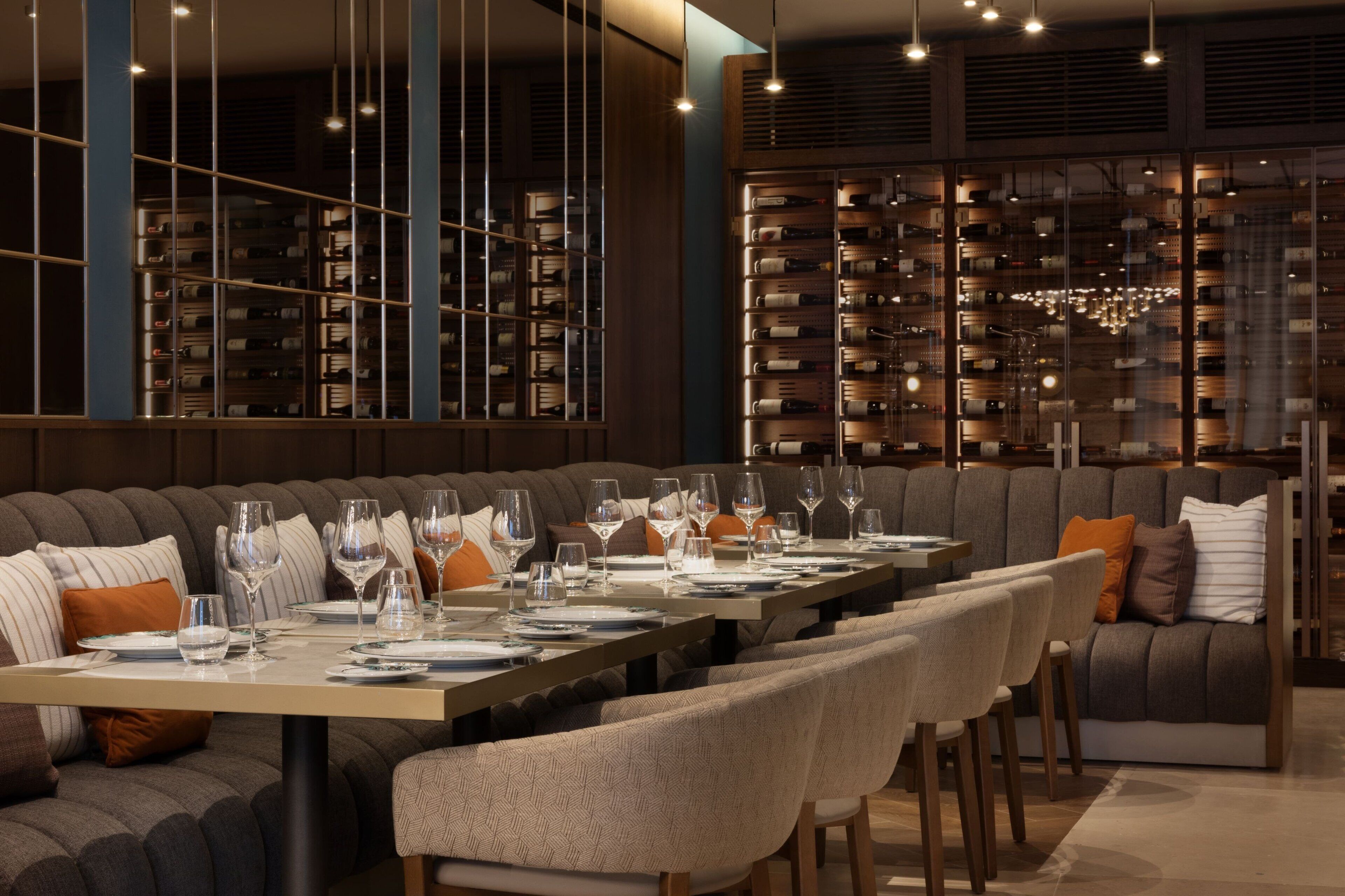 A modern dining area with a long table set for six, surrounded by cushioned seating.