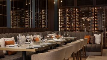 A modern dining area with a long table set for six, surrounded by cushioned seating.