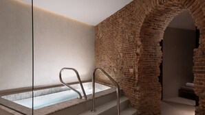 A spa area with a glass-enclosed hot tub, metal stairs, and a brick wall archway. - JW Marriott Hotel Madrid (Madrid)