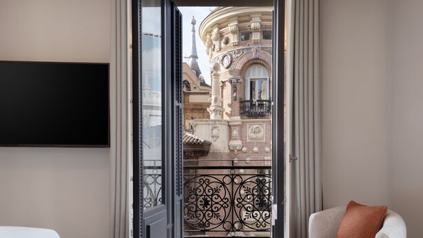 A room with a balcony, a white chair, and a TV mounted on the wall. - JW Marriott Hotel Madrid (Madrid)