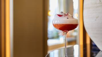 A cocktail in a glass with a frothy top, garnished with herbs, on a reflective surface.
