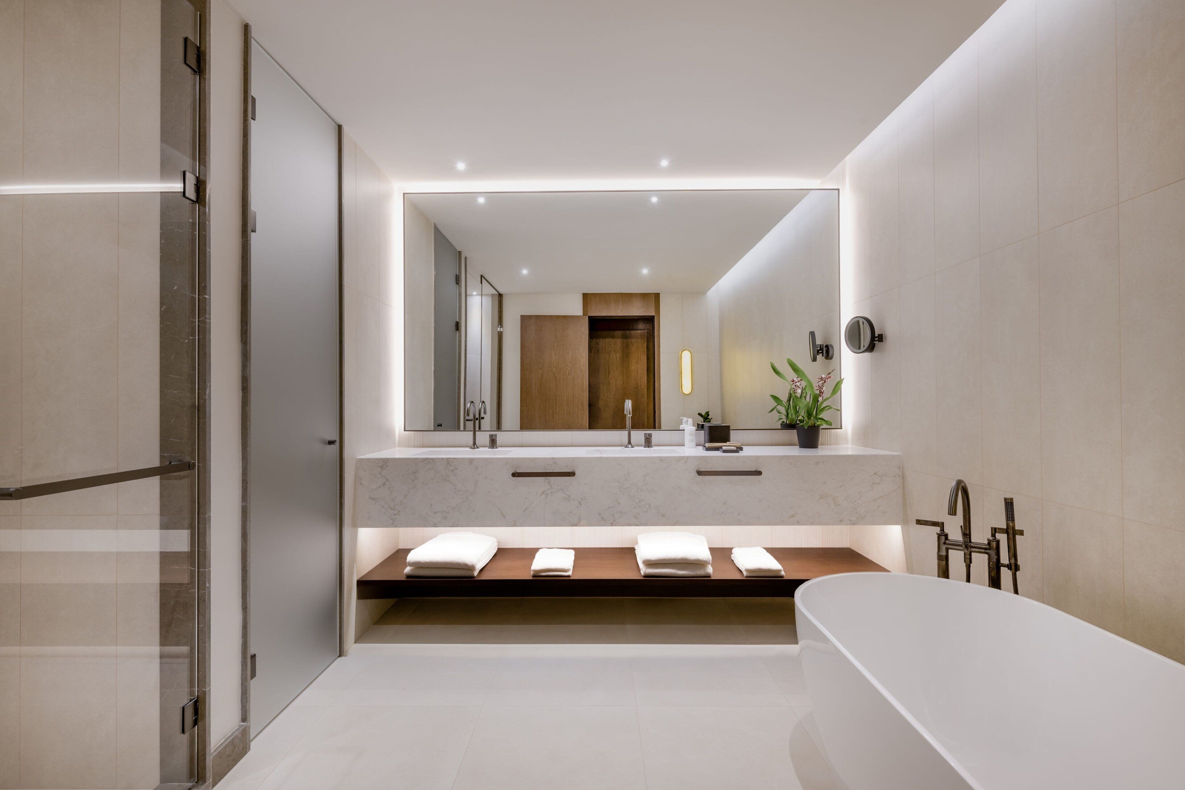 A modern bathroom with a large mirror, two sinks, a bathtub, and a shower area.