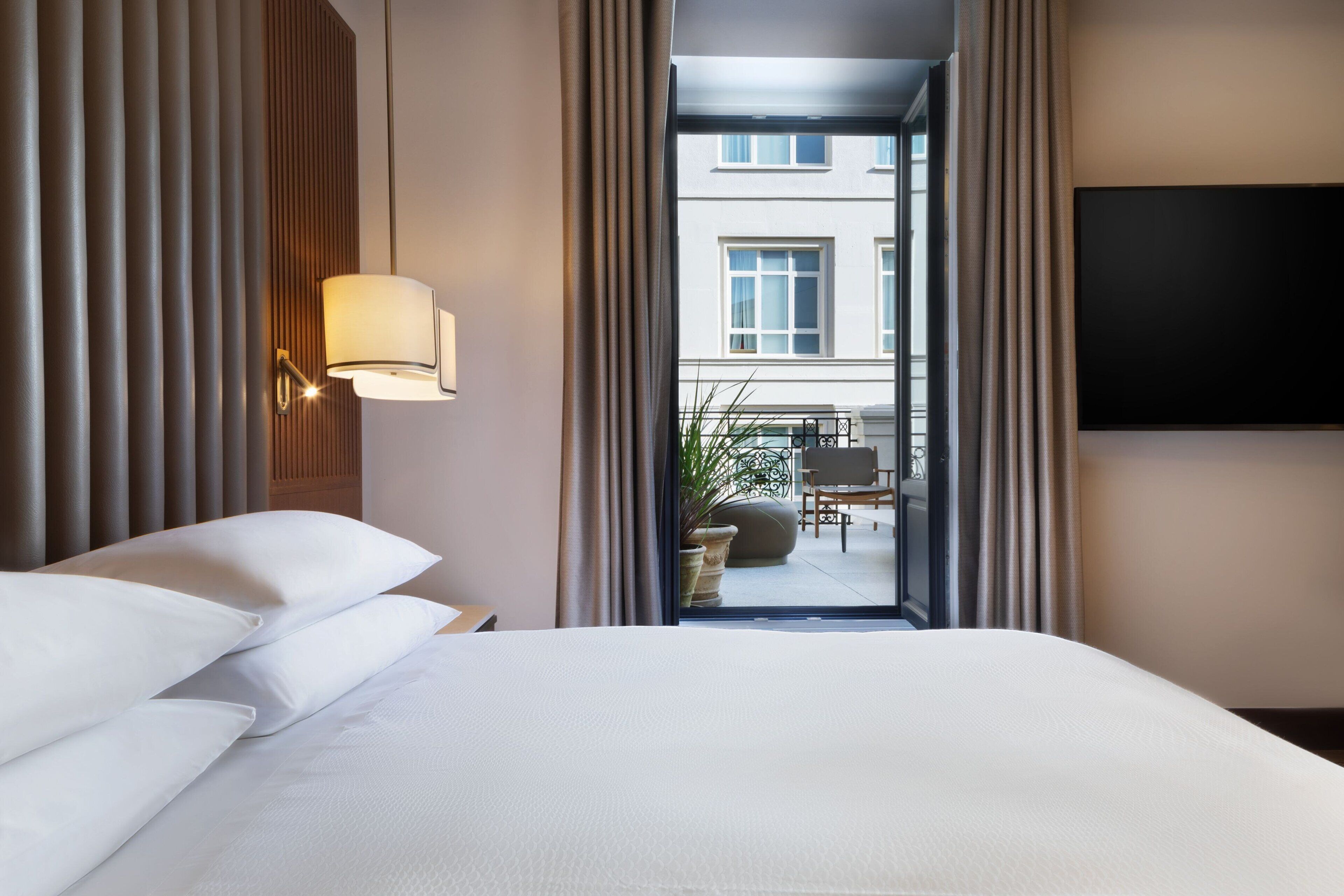 Een hotelkamer met een bed, een lamp, een televisie en uitzicht op het buitenbalkon.