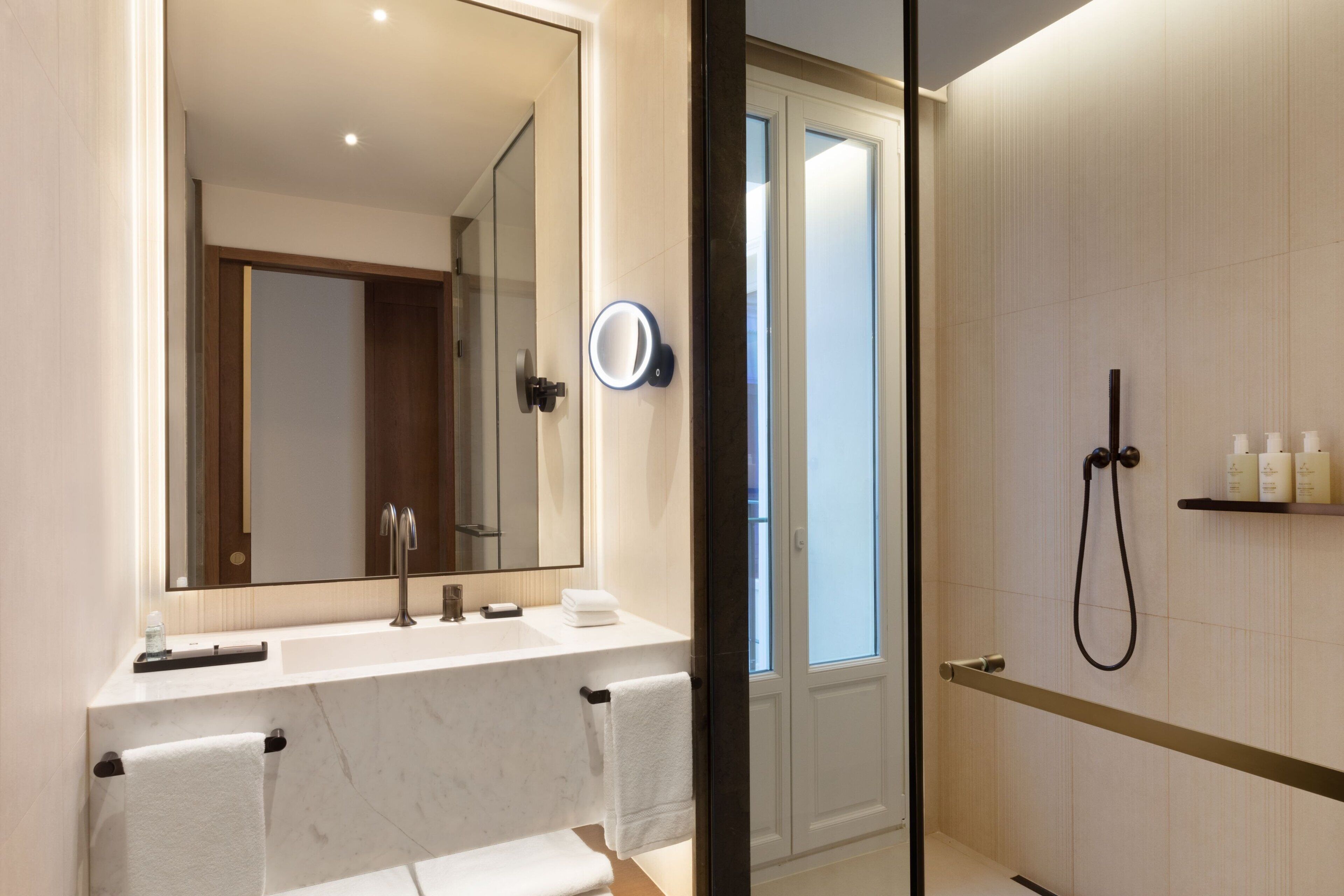 A modern bathroom with a large mirror, a sink, a shower, and a glass door leading to a balcony.