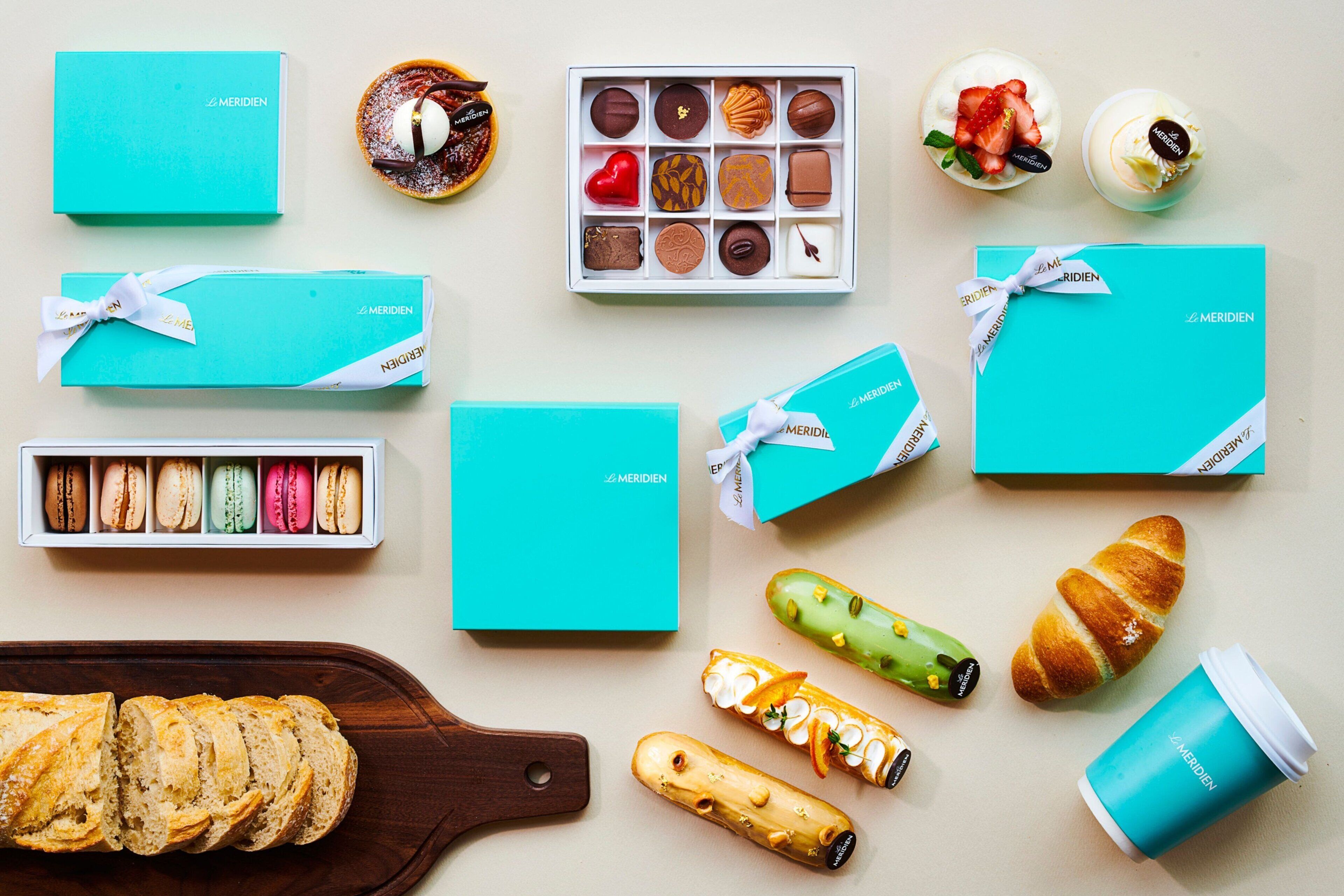 Verschiedene Speisen, darunter Gebäck, Macarons und ein Brotlaib, sind auf einem Tisch angerichtet.