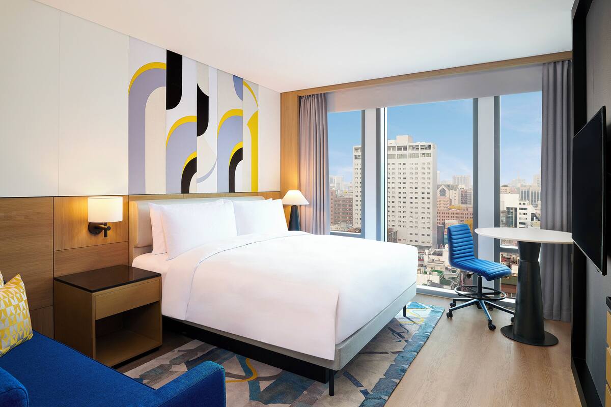 A hotel room with a large bed, a desk, a chair, and a TV.