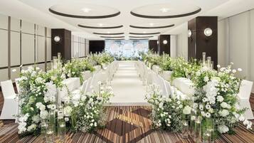 A long banquet table with white chairs, surrounded by floral arrangements and tall glass vases.