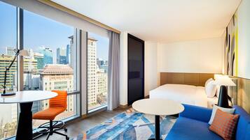 Une chambre d’hôtel avec une grande fenêtre, un lit, un canapé bleu, une petite table et une chaise.