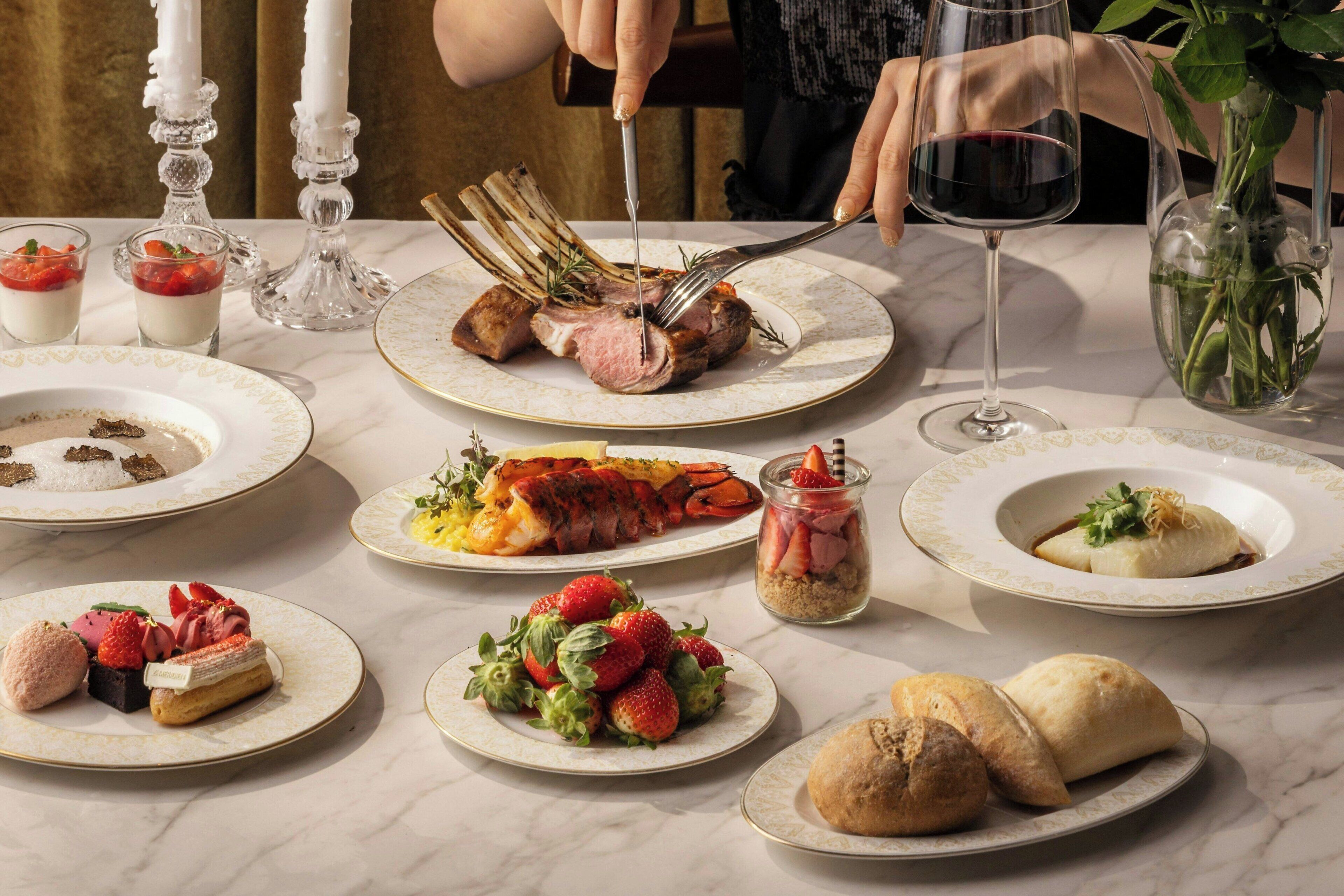 Una mesa servida con diversos platos, incluyendo una cola de langosta, fresas y panecillos.