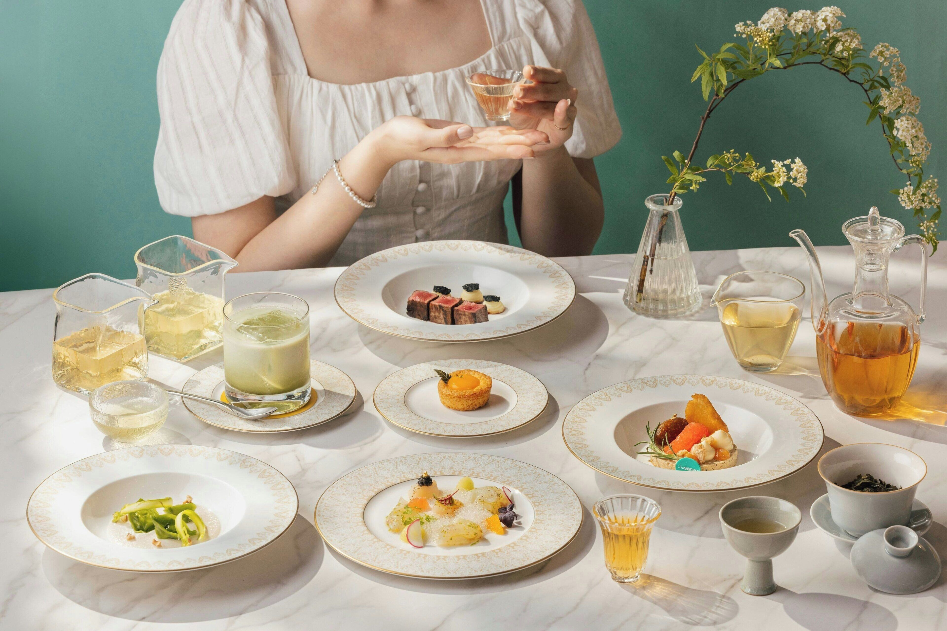 A table set with various dishes and drinks, including a pitcher of tea, a glass of white wine, and plates of food.