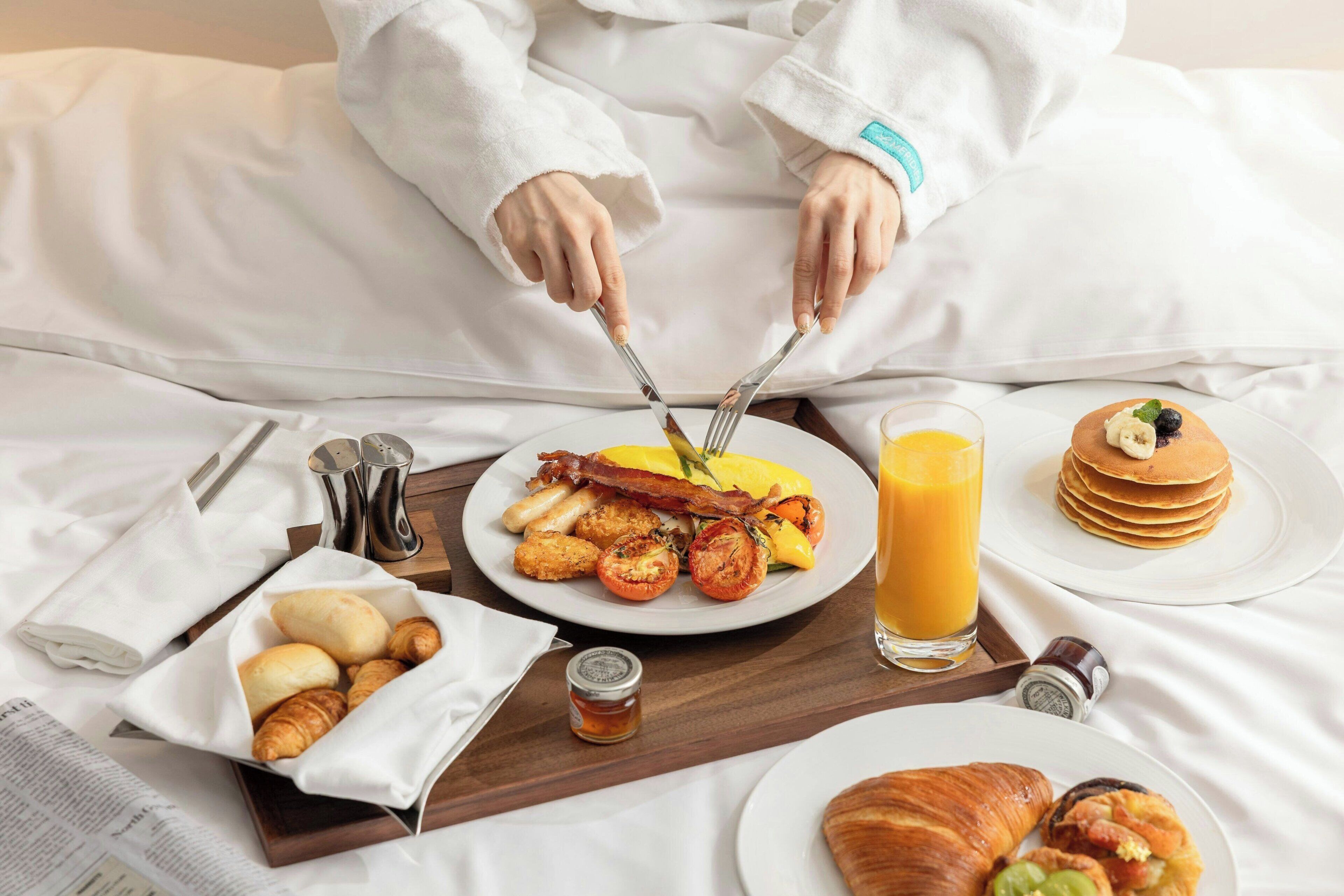 A breakfast tray with croissants, a plate of eggs, bacon, tomatoes, and a glass of orange juice.