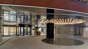 Un vestíbulo moderno con piso reflectante circular, una columna central grande y una entrada de vidrio con puerta cerrada.