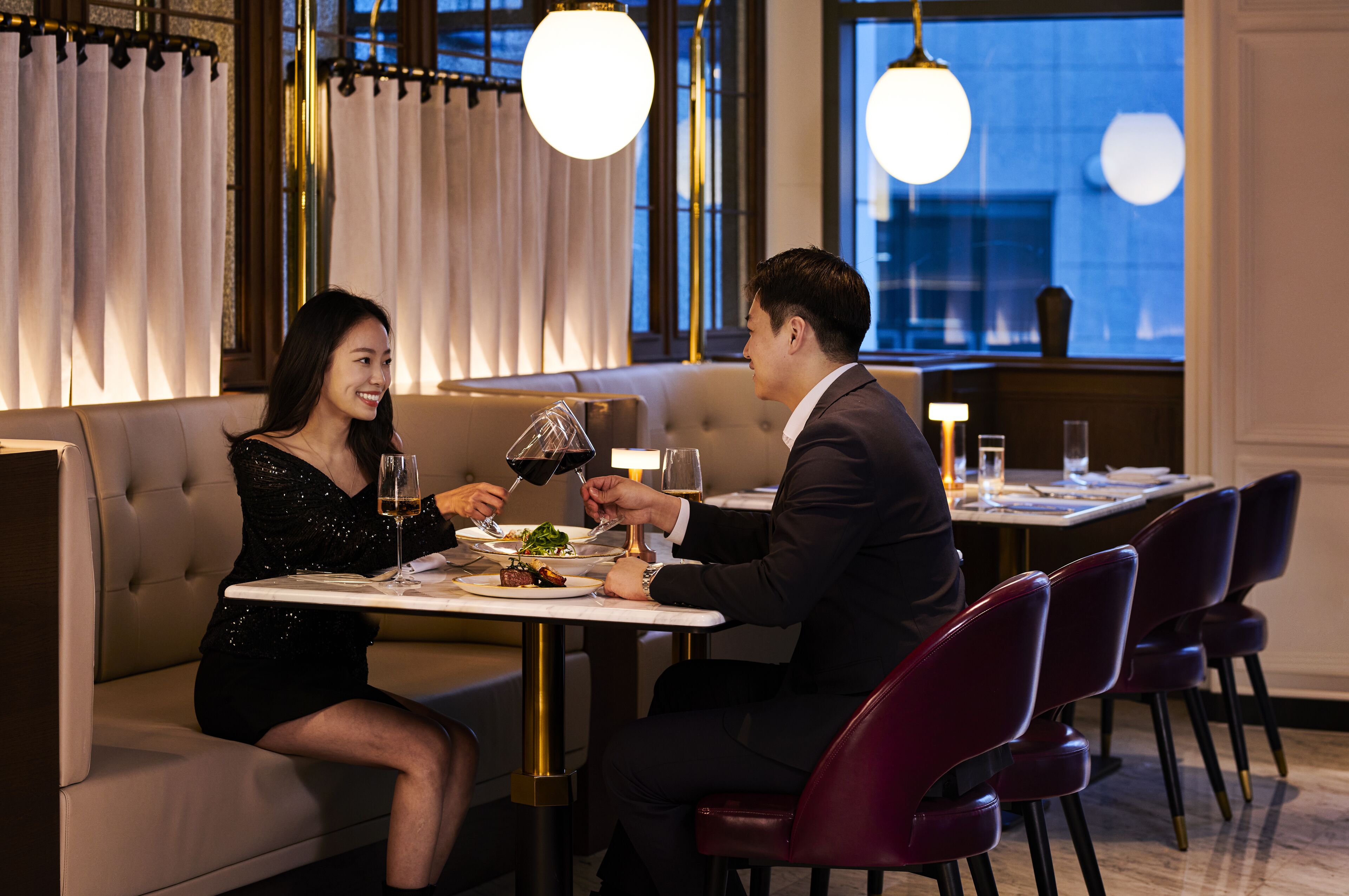 A couple dining at a table in a modern restaurant with a view of the city at night.