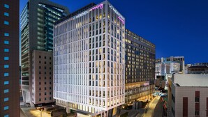 Un hotel moderno con fachada de diseño geométrico, ventanas amplias y un letrero de neón en la parte superior.