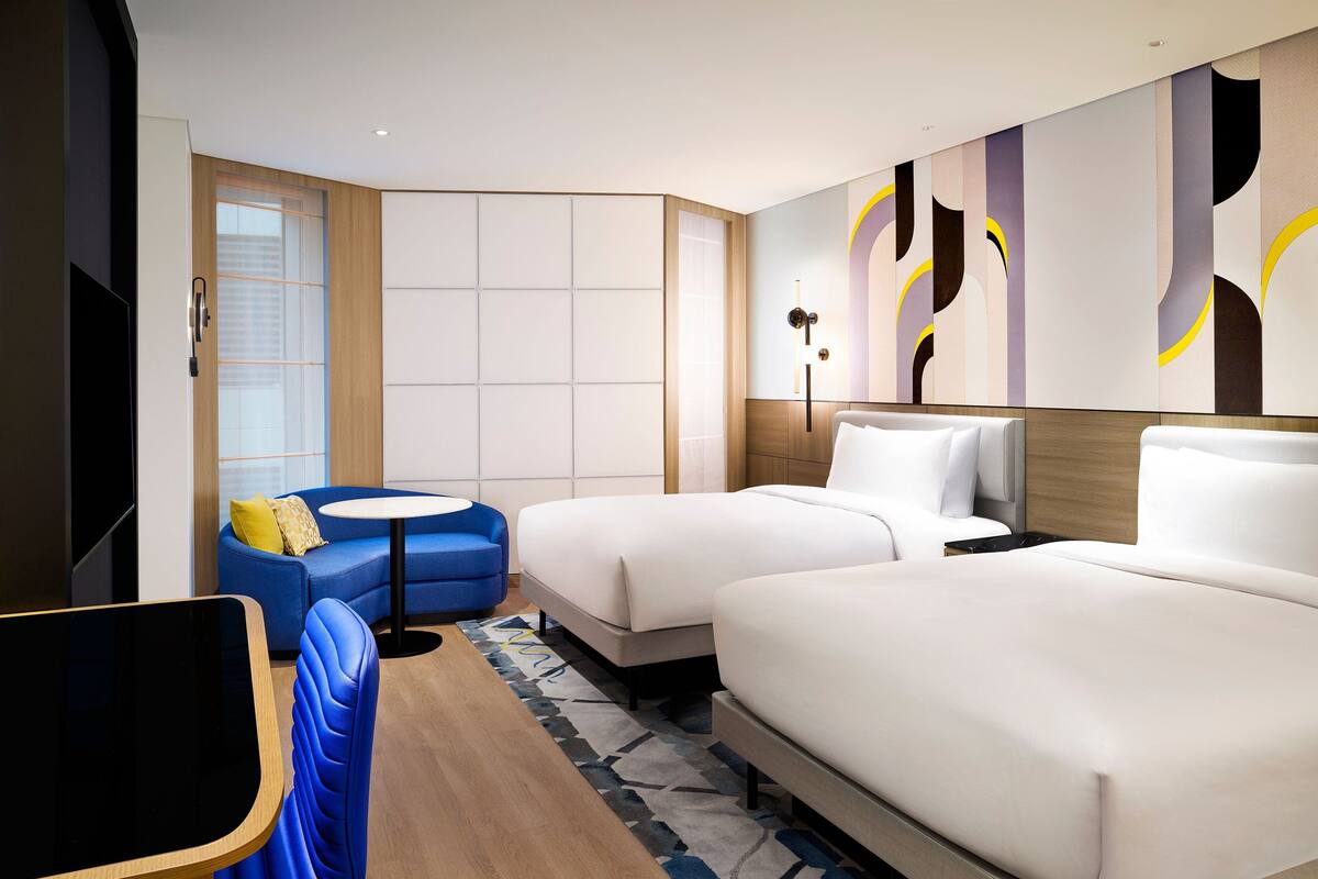 A hotel room with two beds, a blue sofa, a small round table, and a TV.