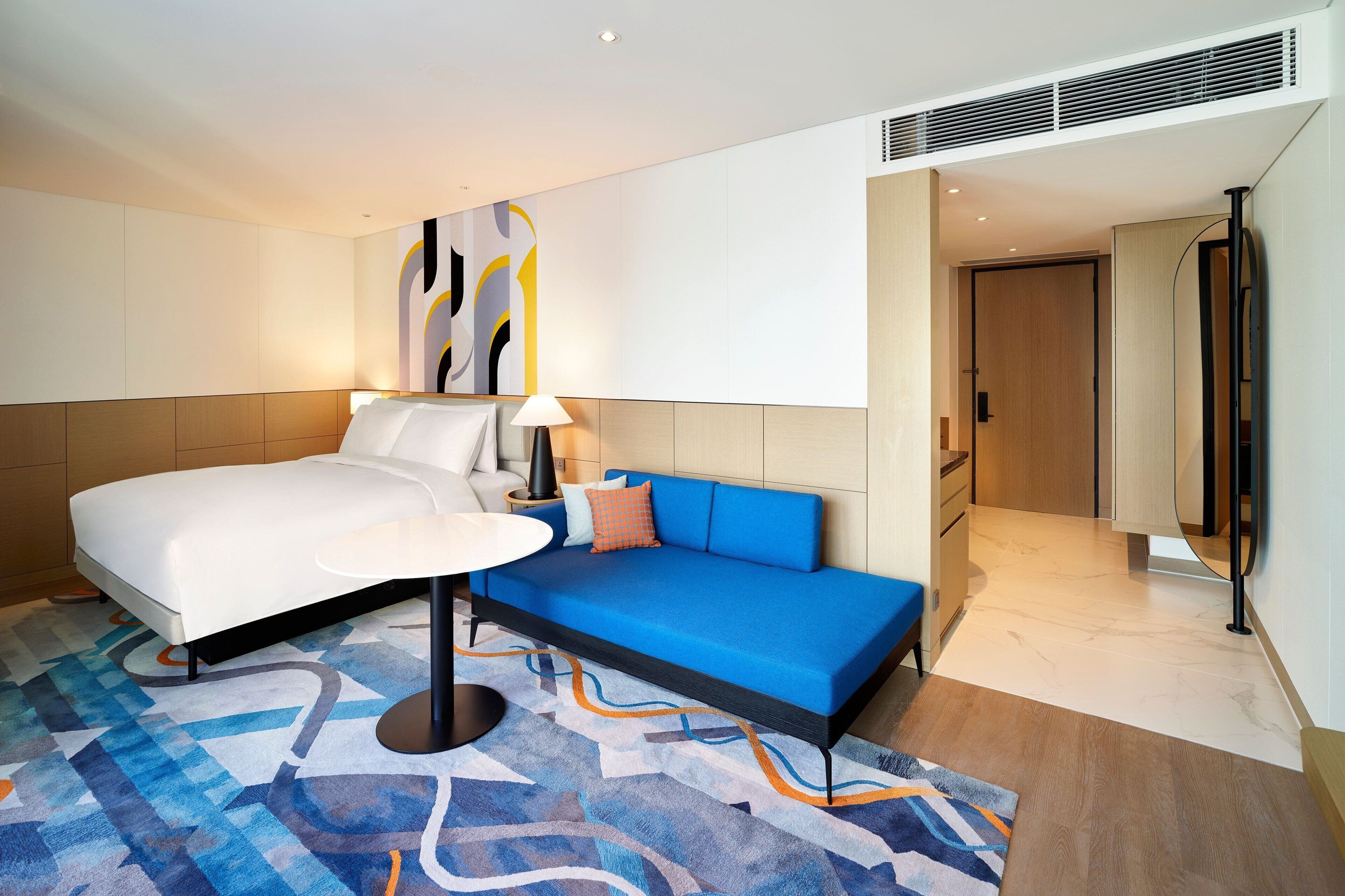 A hotel room with a bed, a sofa, a small table, and a lamp.