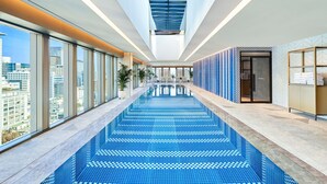 Piscina interior moderna con vistas a la ciudad, amplias ventanas y suelo de baldosas.