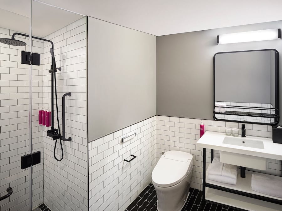 Ein modernes Badezimmer mit einer weißen Duschkabine, einem weißen Waschbecken mit schwarzem Wasserhahn und einem Spiegel darüber.