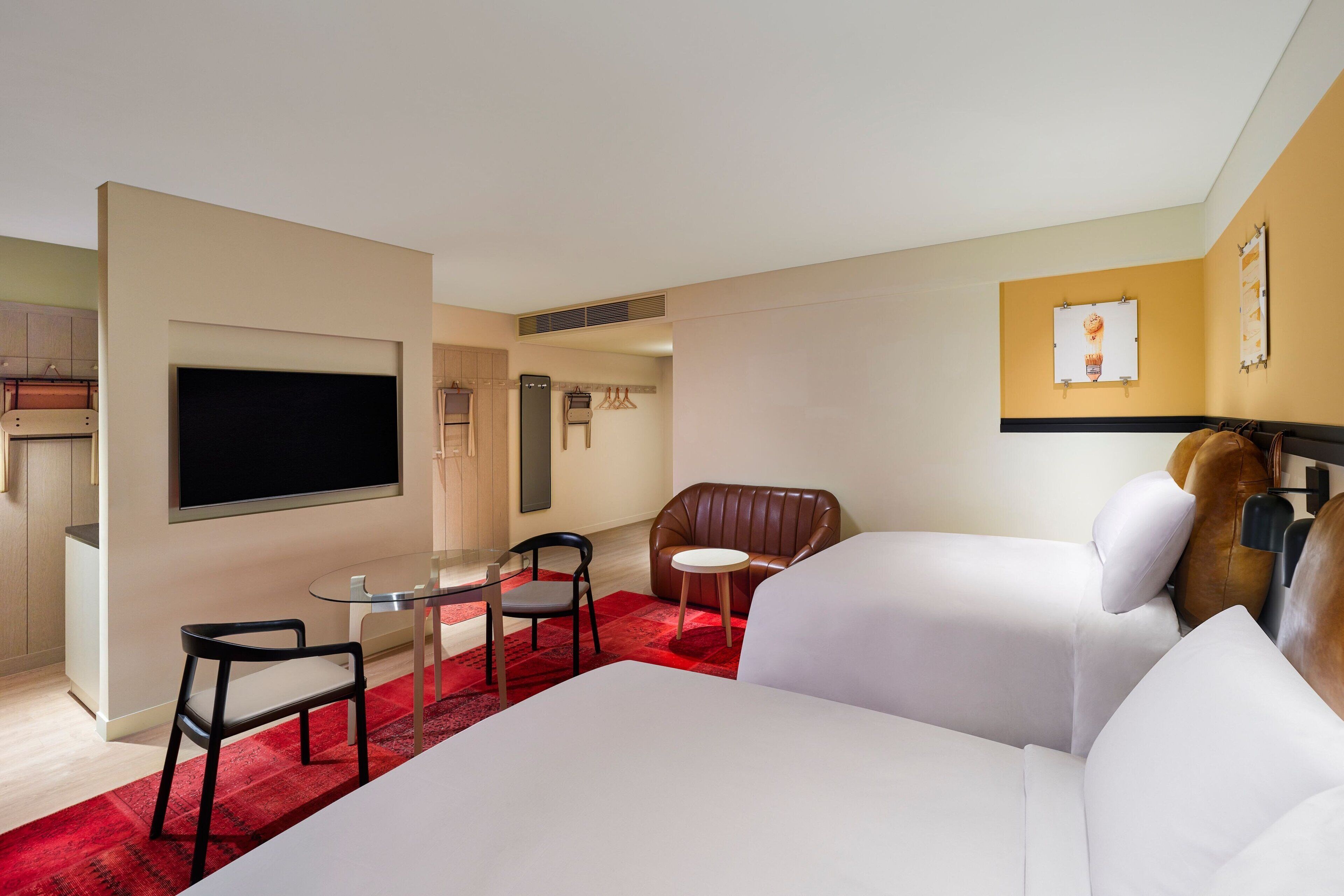 Ein Hotelzimmer mit einem großen Bett, einem Fernseher, einem Esstisch mit Stühlen, einem roten Teppich und einer Ledersofa.