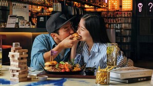 A couple dining at a bar with a board game, a drink, and books on the table. - Moxy Seoul Myeongdong (Seoul)