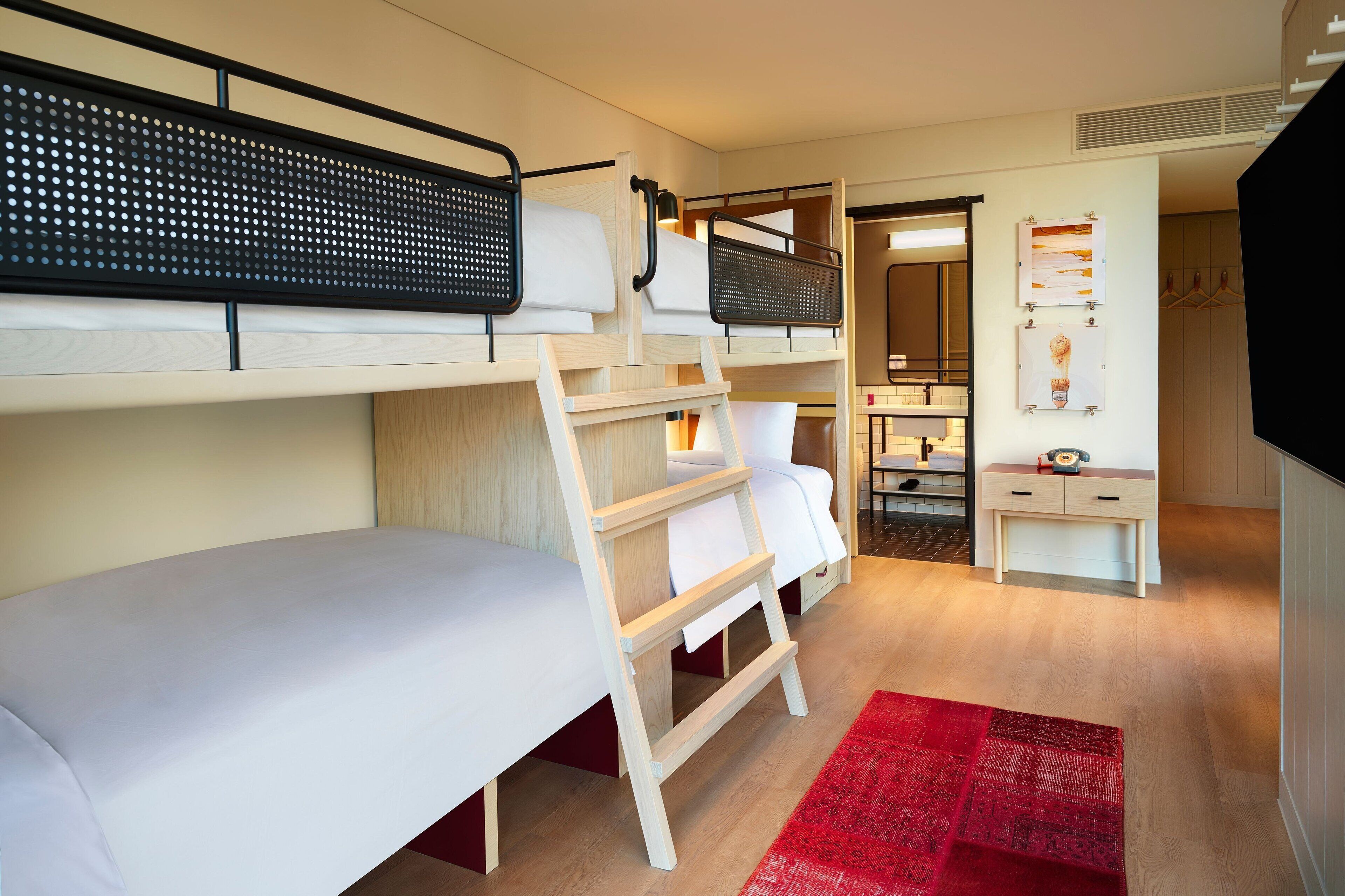 A compact hotel room with bunk beds, a small desk, a mirror, and a red rug.