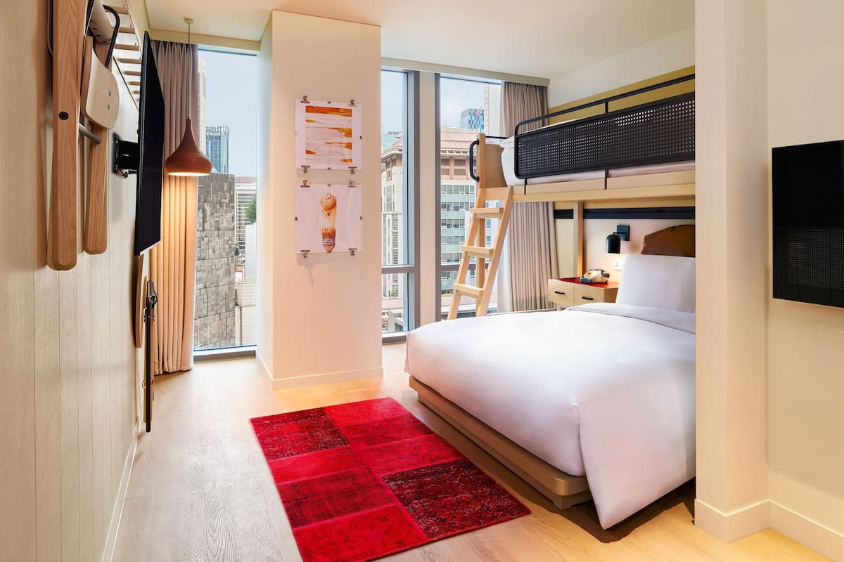 Una habitación de hotel moderna con una cama grande, una alfombra roja, un televisor y un balcón con vistas a la ciudad.