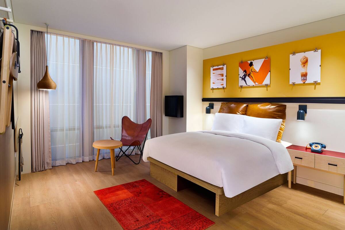 Una habitación de hotel con una cama grande, un tapete rojo, un escritorio de madera, una silla y un televisor en la pared.