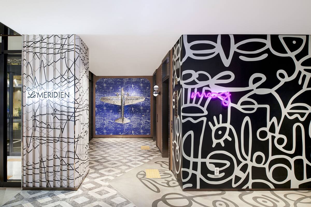 Vestíbulo de hotel con suelo de diseño geométrico, pared con mural de paisaje urbano y panel decorativo con diseños abstractos.