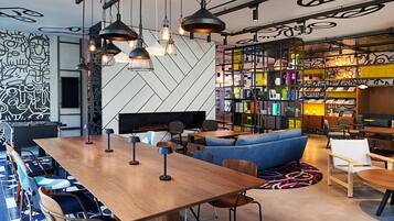 A modern lounge area with a long wooden table, blue seating, and a bookshelf filled with books and decorative items.