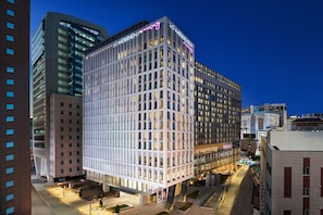 A modern hotel with a grid-like facade, large windows, and a neon sign.