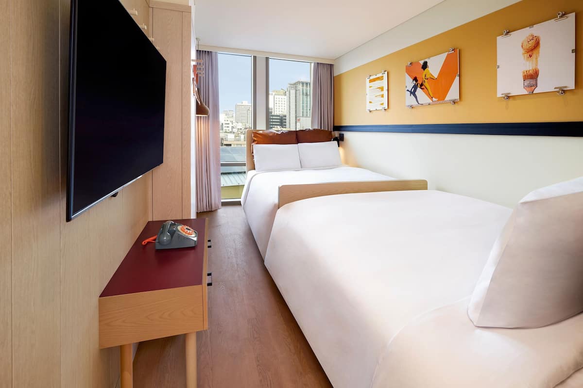 Habitación de hotel con cama, escritorio, teléfono, televisor y obras de arte en la pared.