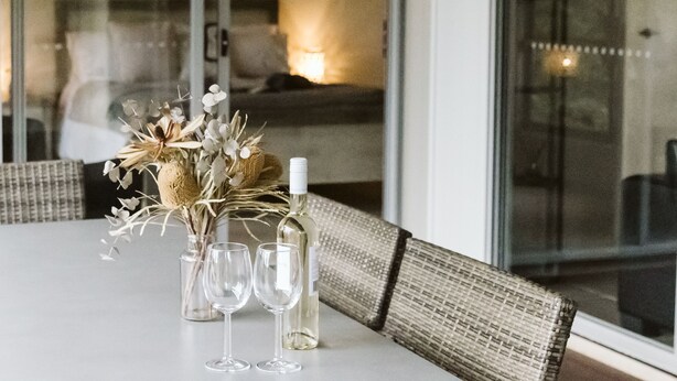 A dining table with a vase of flowers, a bottle of white wine, and two empty wine glasses. - Kookaburra - Private One Bedroom Cottage with Lake View (North Maleny)