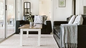 A modern living room with a sofa, a coffee table, and a potted plant. - Kookaburra - Private One Bedroom Cottage with Lake View (North Maleny)