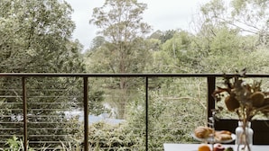 A balcony with a view of a forested area, a table with a plate of food, and a vase with dried flowers. - Kookaburra - Private One Bedroom Cottage with Lake View (North Maleny)