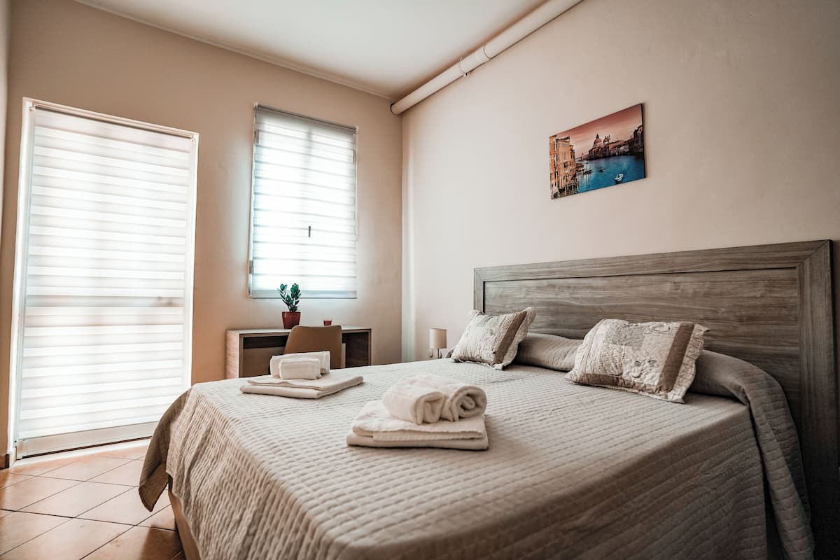 A neatly made bed with a rolled towel, a bedside table with a lamp, and a painting on the wall.