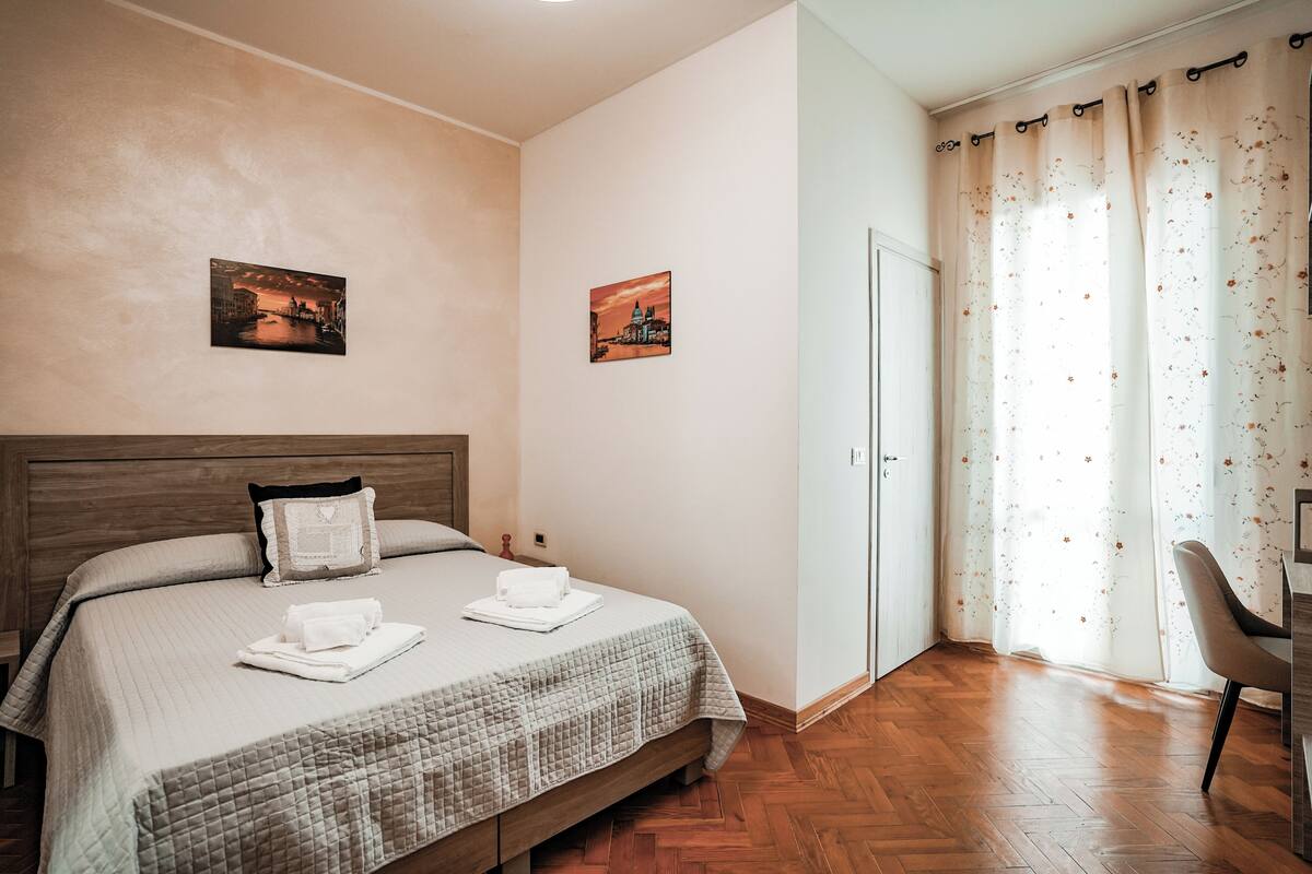 A neatly made bed with a quilt, two pillows, and folded towels. There are two framed pictures on the wall.