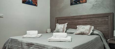 A neatly made bed with folded towels, a wooden headboard, and two paintings on the wall.