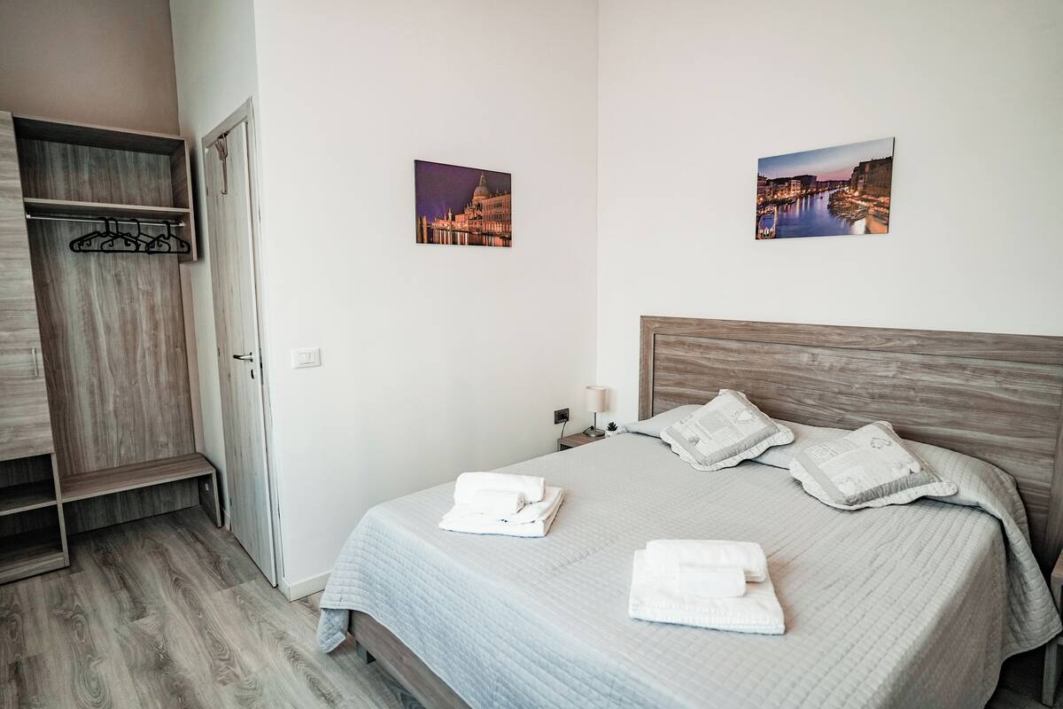 A bedroom with a bed, a wooden wardrobe, and two framed pictures on the wall.