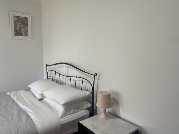 Een bed met witte beddengoed, een zwart metalen hoofdbord en een nachtkastje met een lamp.