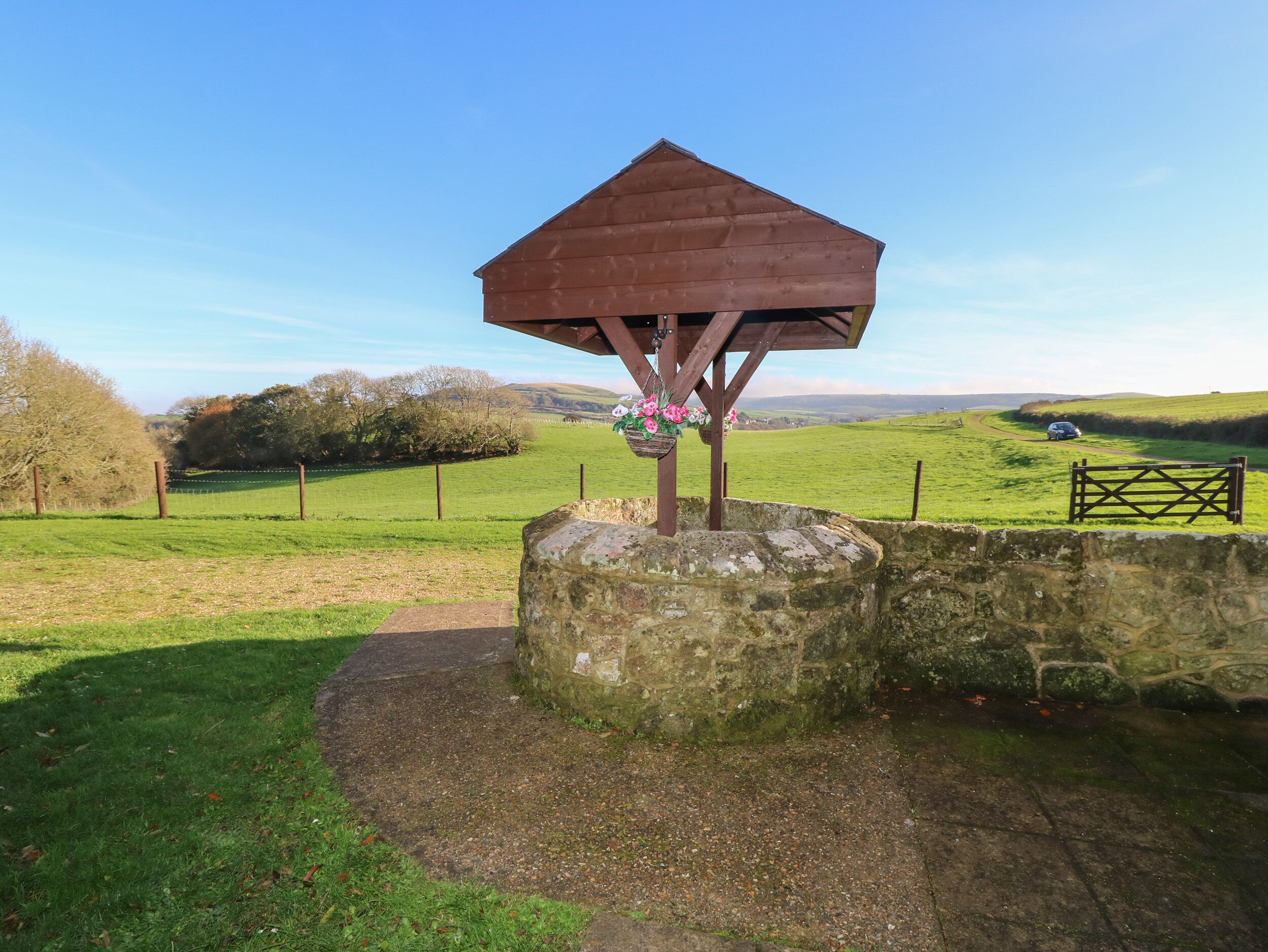 A stone structure with a wooden shelter, surrounded by a stone wall and a grassy field.