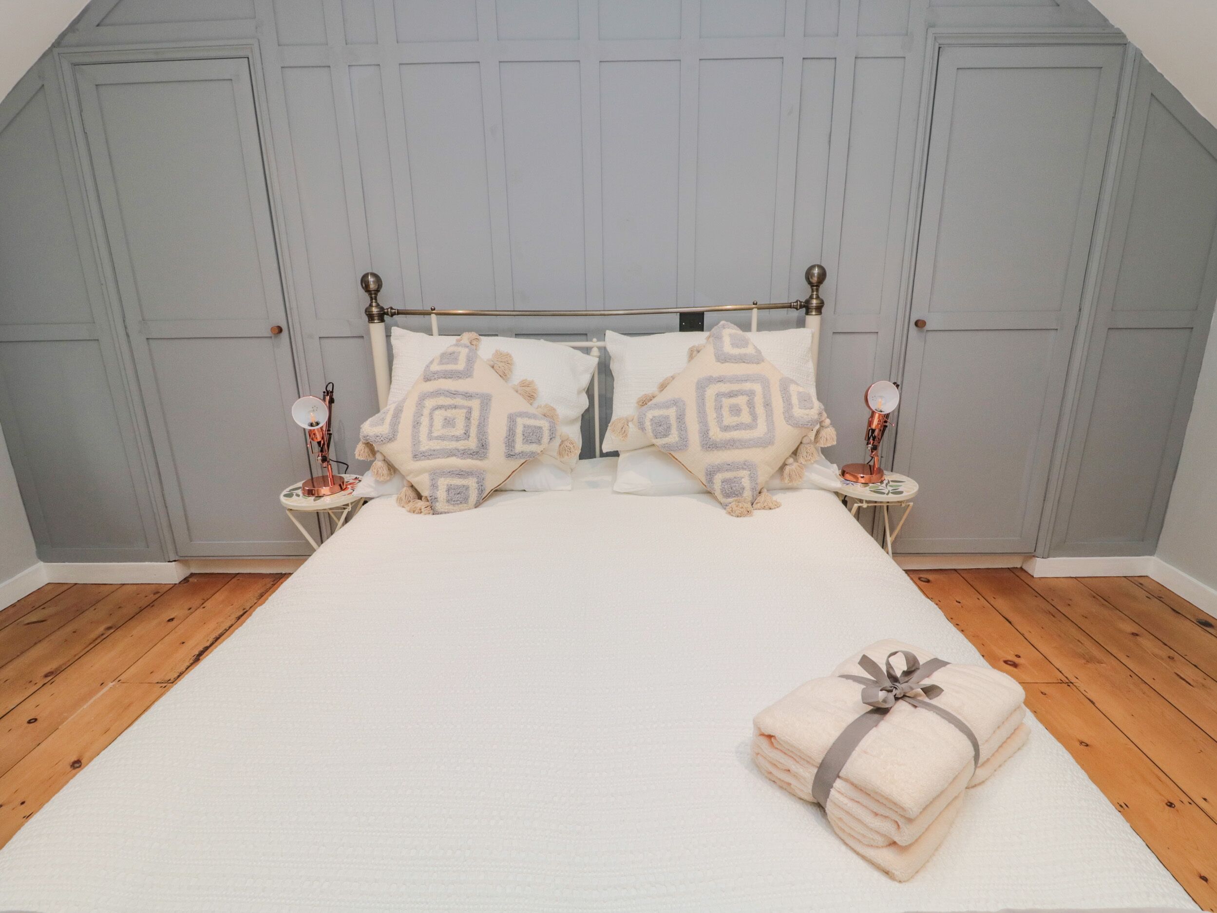 A neatly made bed with patterned pillows, a bedside table with a lamp, and a folded towel on the floor.