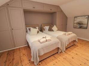 A bedroom with two beds, wooden flooring, and built-in wardrobes. - Donni Hall Cottage (Chathill)