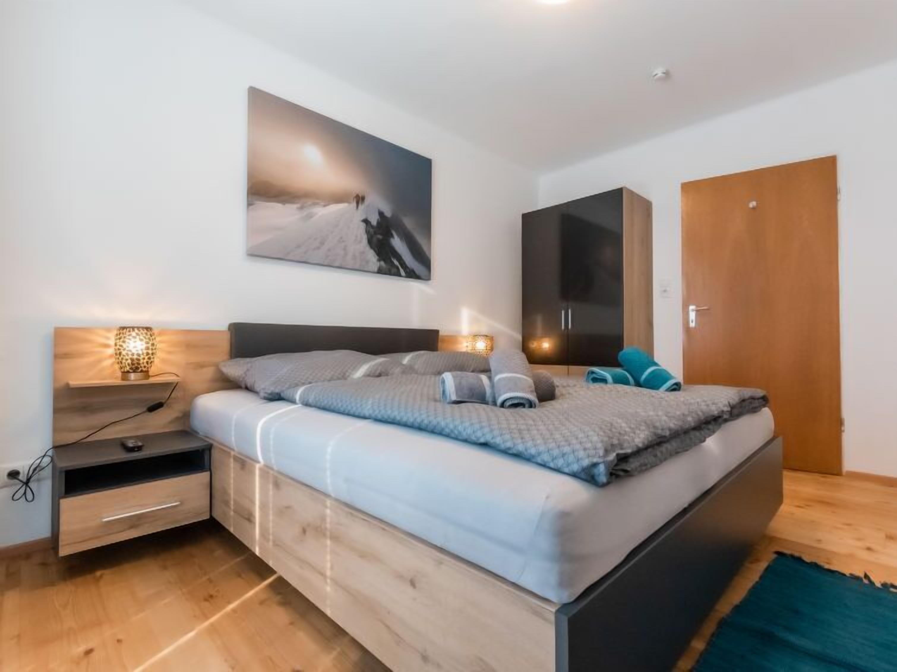 A modern bedroom with a bed, bedside tables, a wardrobe, and a painting on the wall.