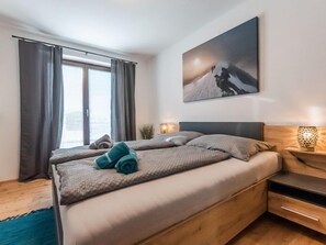 A modern bedroom with a large bed, a nightstand, a lamp, and a painting on the wall.